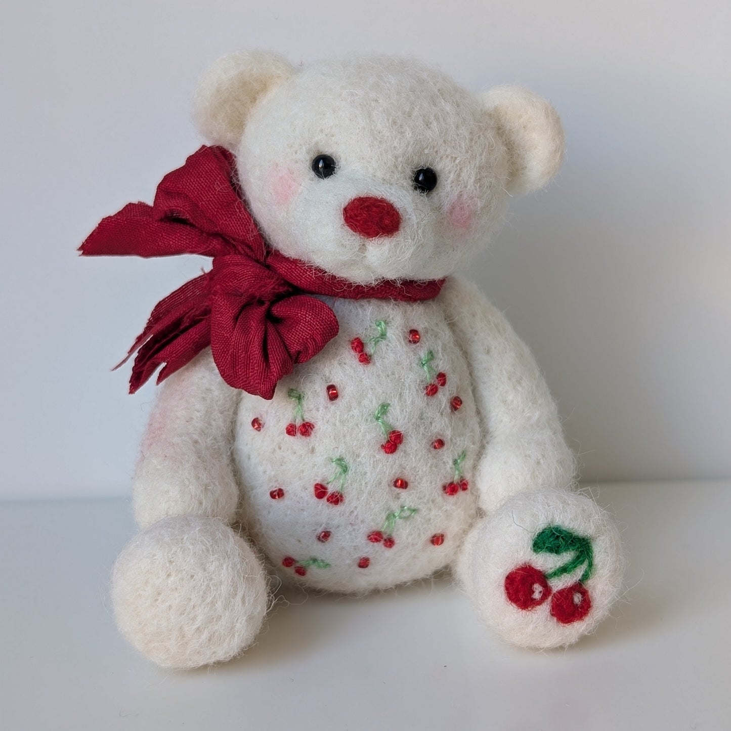 White teddy bear with red bow and cherry designs on a white background